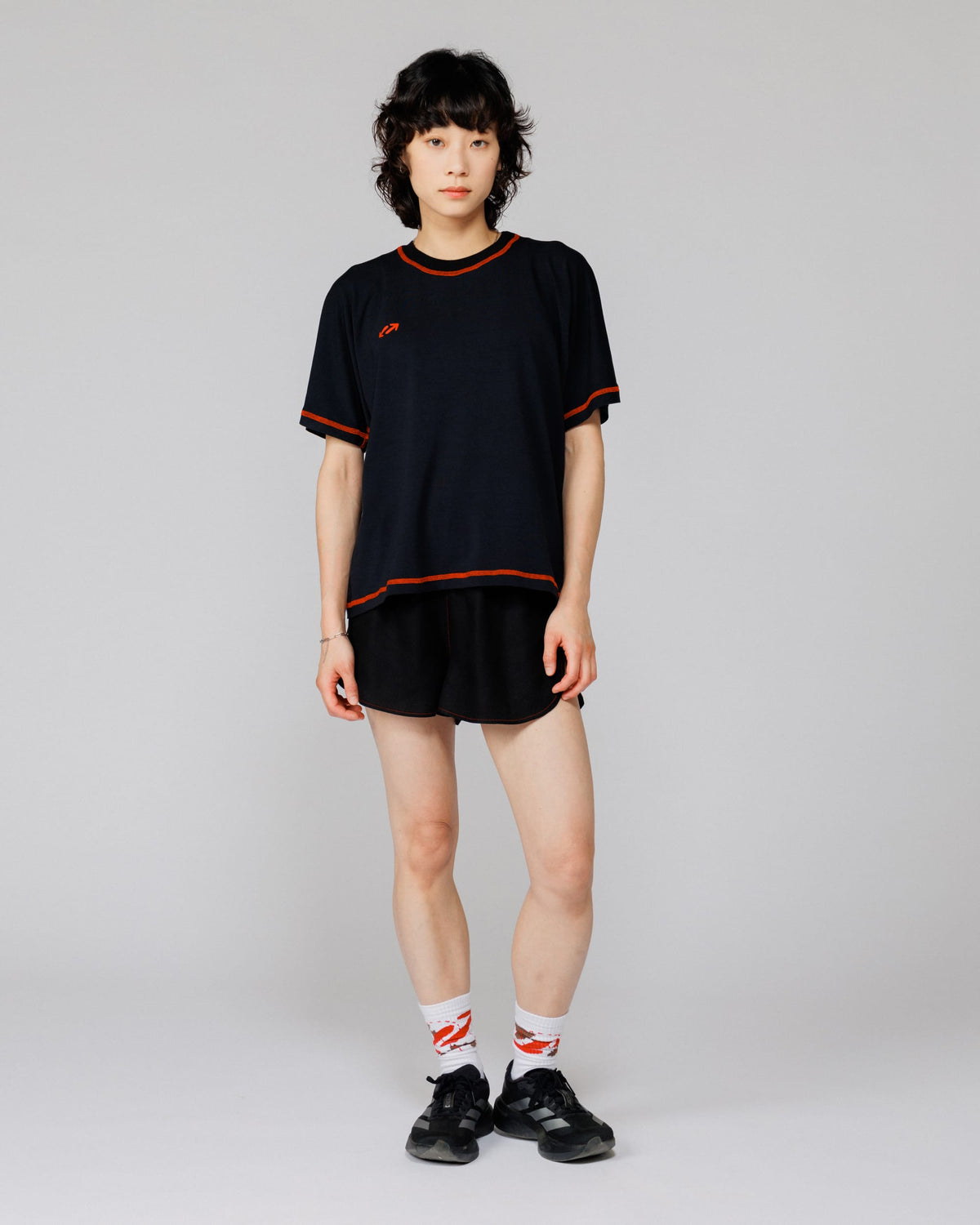 Model wearing Outnback Bog Tee in black, full-length front view with orange contrast overlock stitching